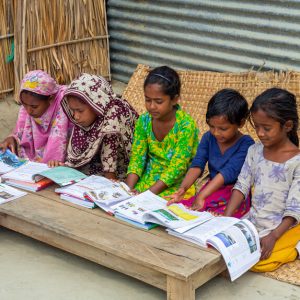 Bangladesh – March 06, 2021: A lady teacher is sitting on the outdoor in front of a house in the village teaching some of the poor children at Majherchor, Chandpur, Chittagong.